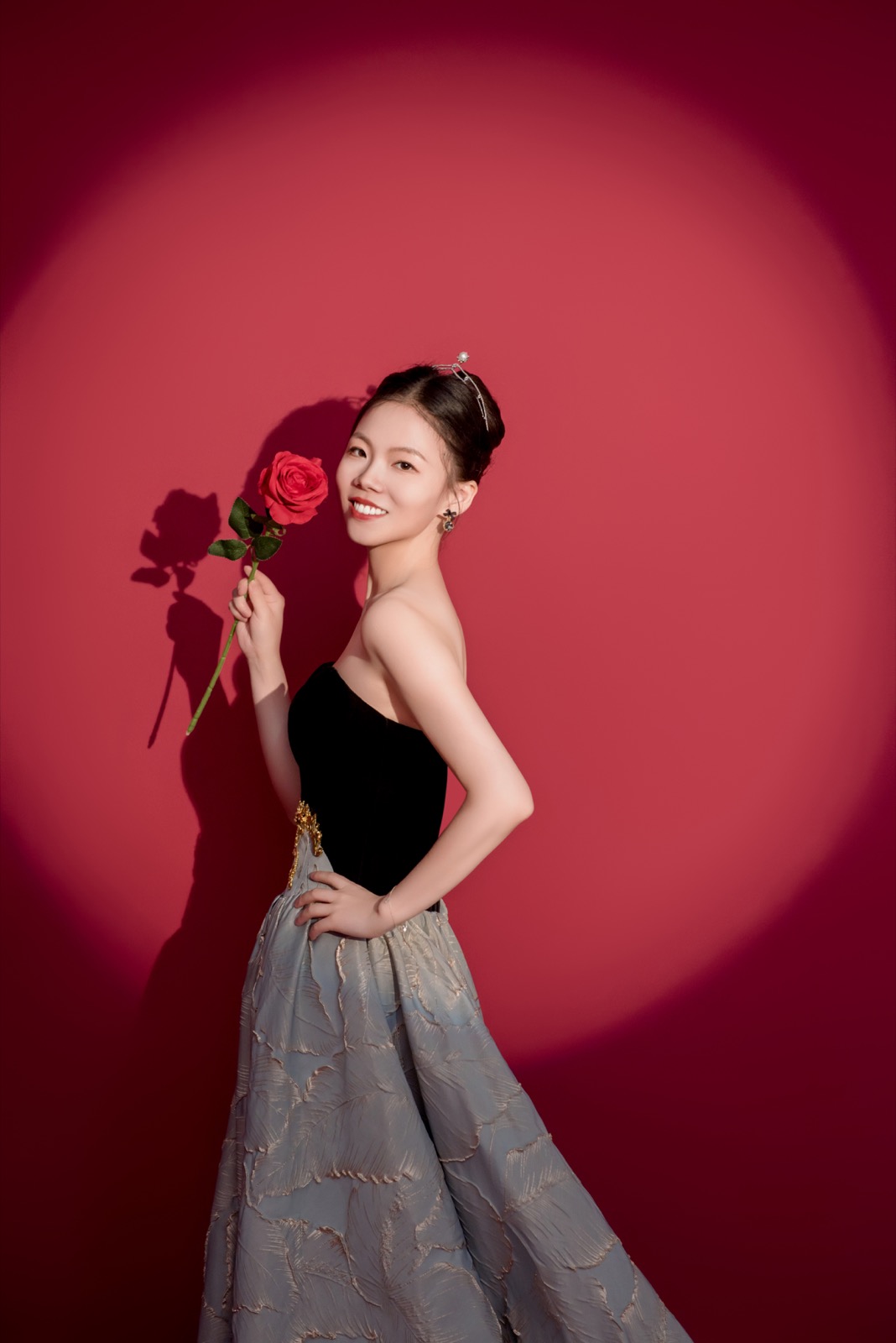 Lucy Xing Wang smiling with a red rose against a red backdrop