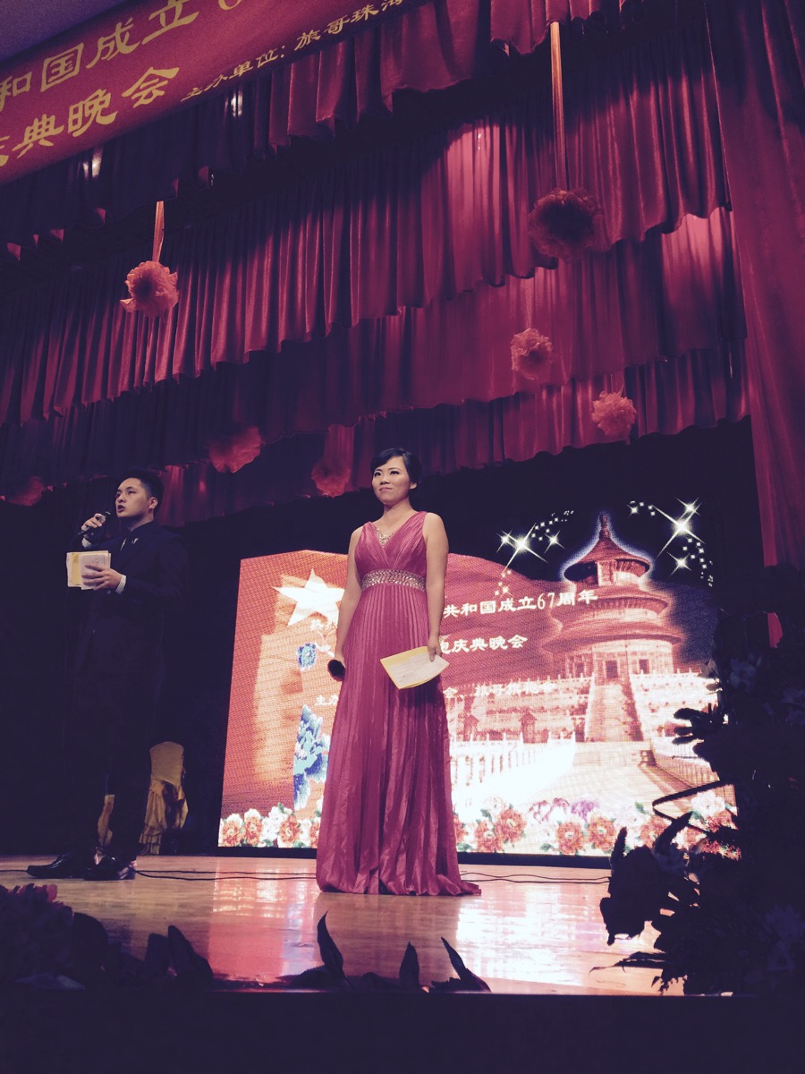 Lucy holding a microphone and notes on stage at a cultural event
